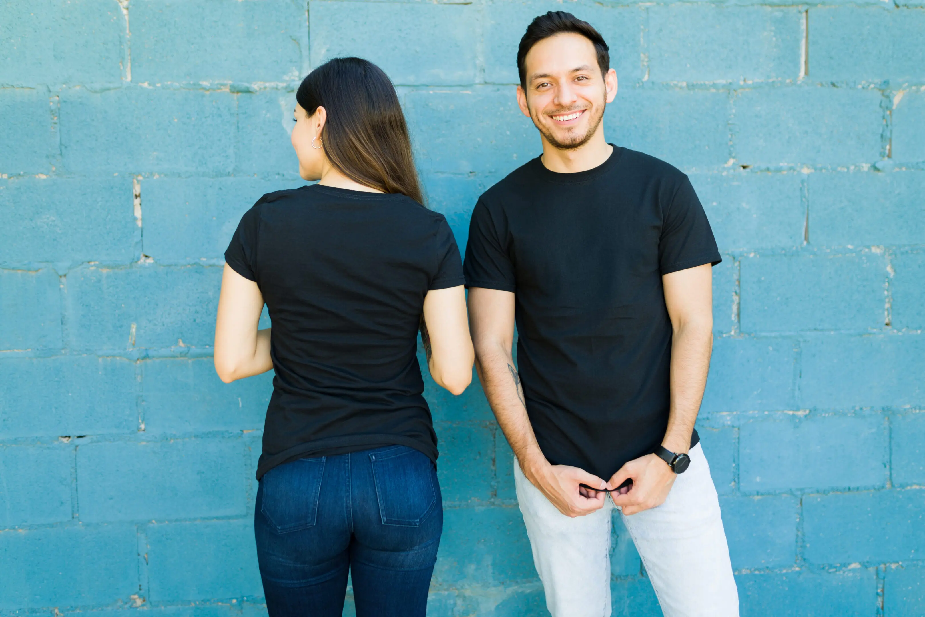 Young woman and man with custom print t-shirts Two people in black shirts, blue wall.