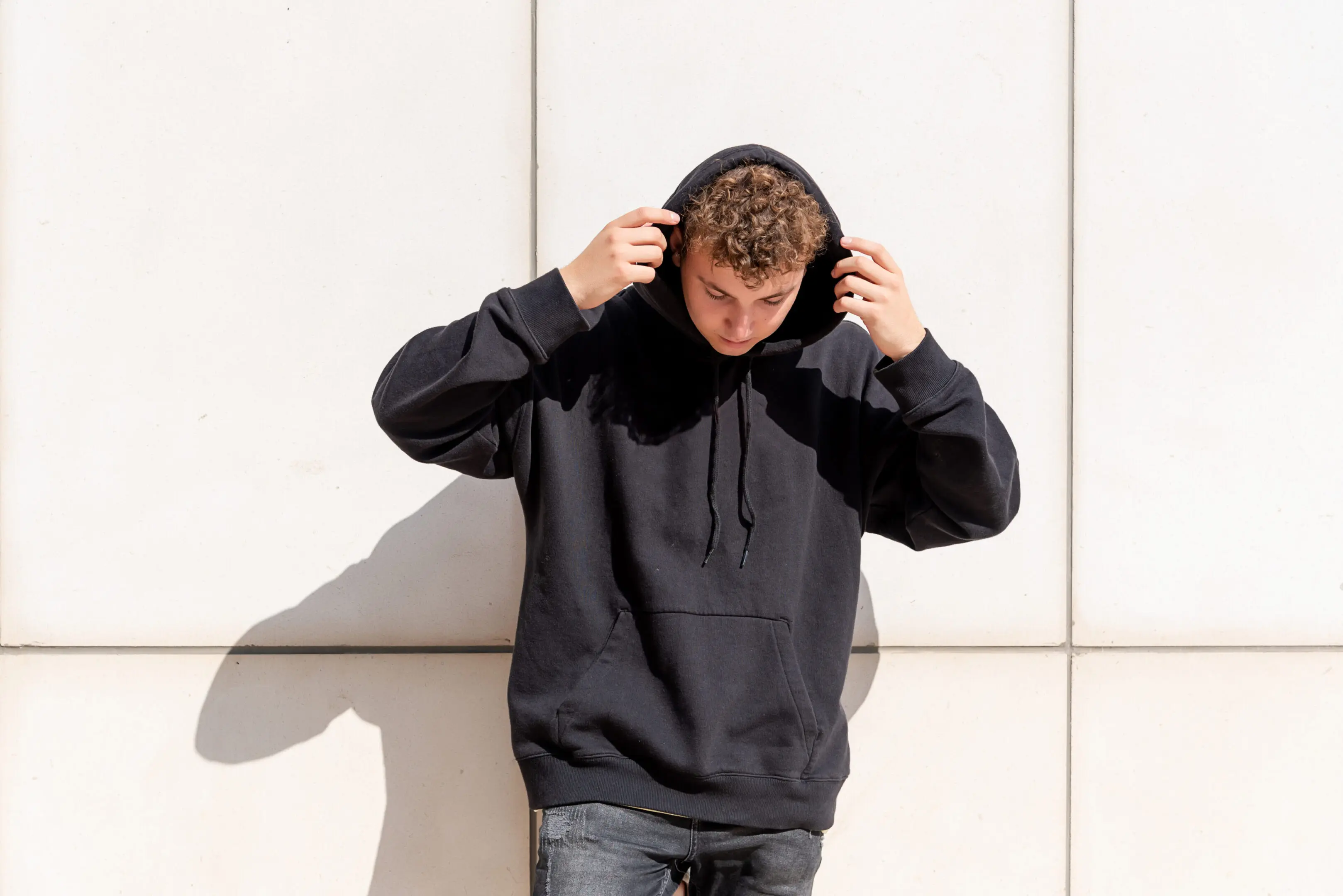 Young man in black sweatshirt putting his hood up on the outside Person wearing black hoodie, adjusting hood.