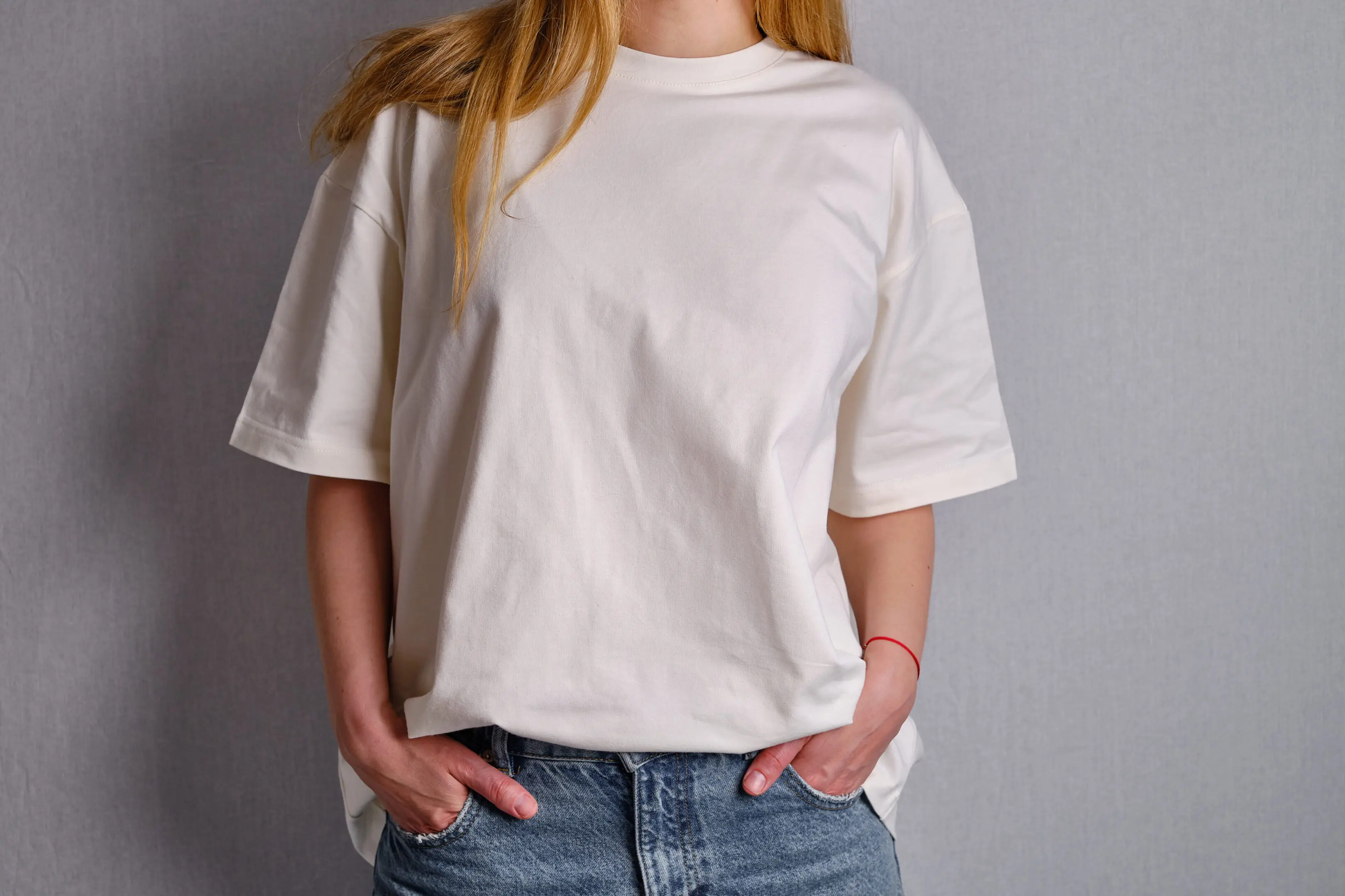 Woman in a white T-shirt poses near a white wall. Hand gestures and emotions. Studio photography. The concept of emotion, strength and fun. Casual wear. Space for inscriptions and logo Person in white t-shirt and jeans.