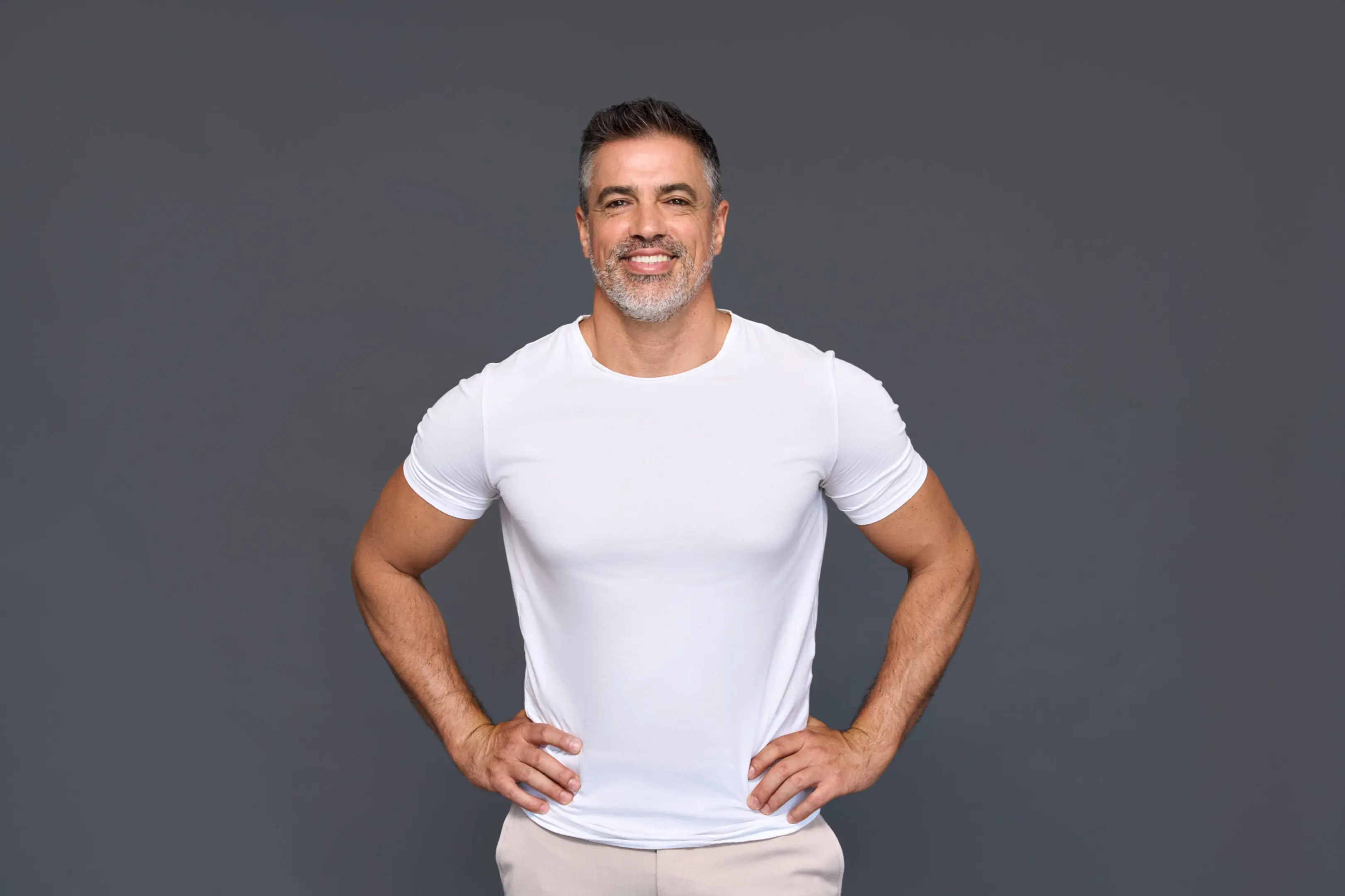 Happy fit sporty mature older man wearing white t-shirt isolated on background. Man in white shirt, gray background, smiling.